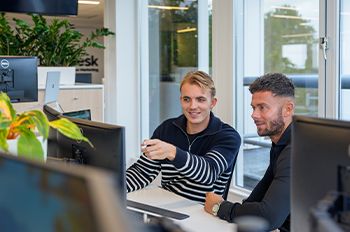 Twee jonge professionals bespreken productdata en duurzaamheid aan een computer, gericht op het Digitaal Product Paspoort.